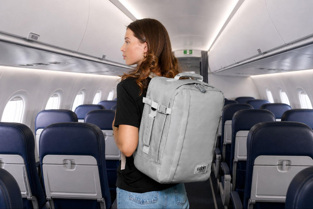 Traveller wearing a single backpack while standing inside an aeroplane cabin.